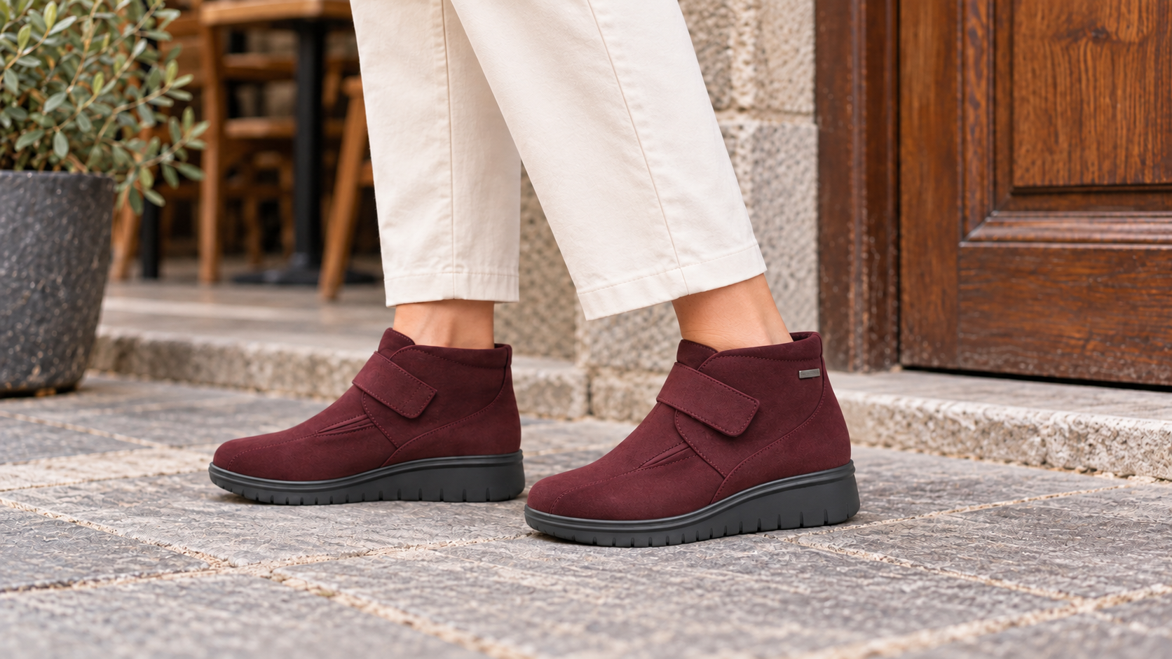 Botines 55353 de ante burdeos con velcro, puestos y con ambos pies apoyados en el suelo.